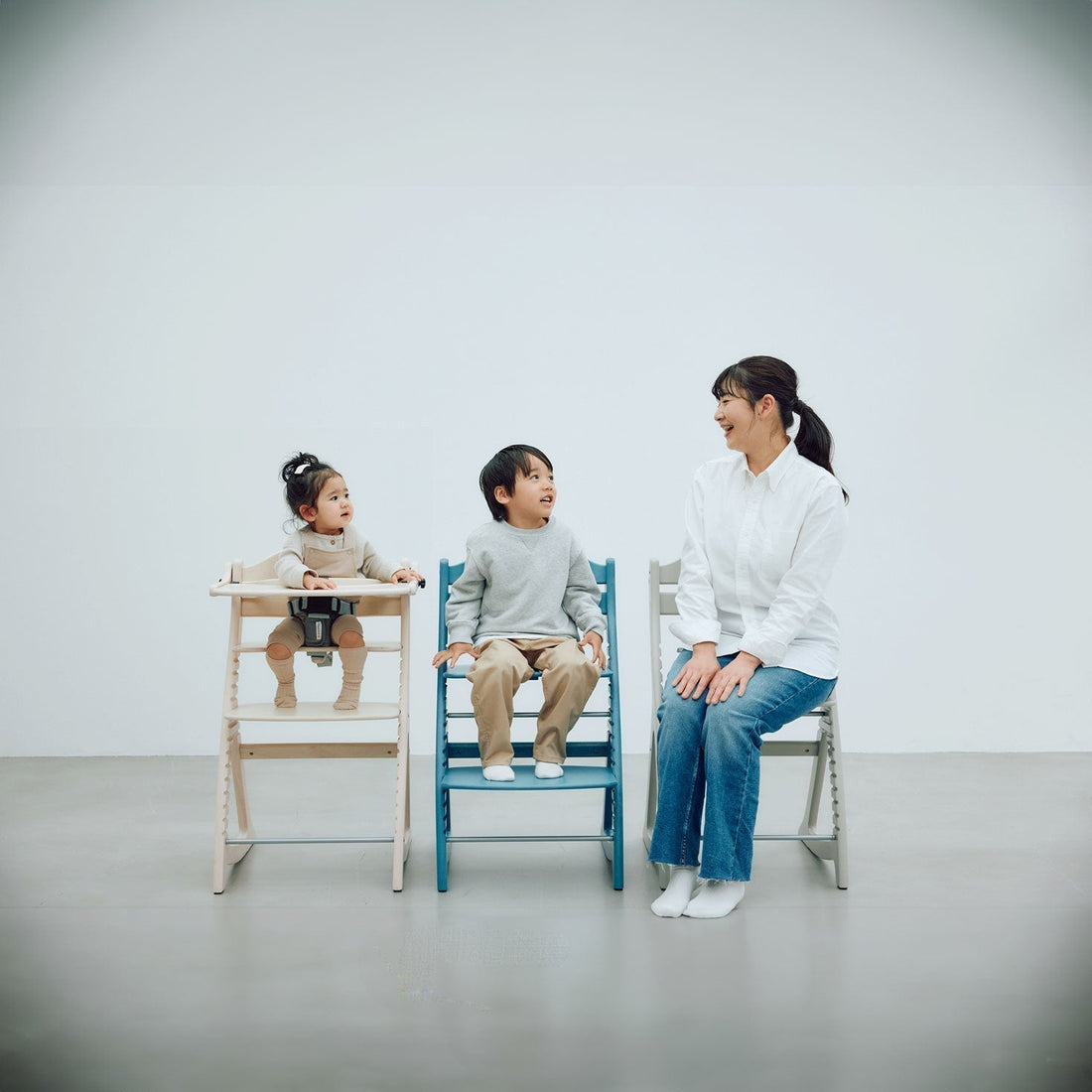 A wooden adjustable highchair at a family dining table, showing the seat and footboard at different height settings as a child grows
